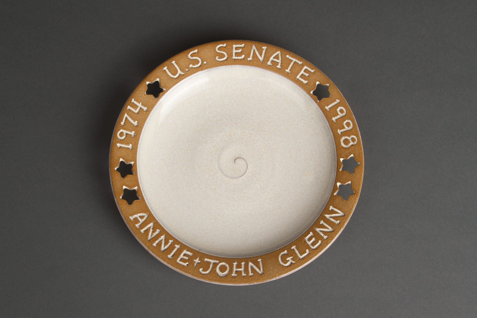 White plate with tan border inscribed with 1974 U.S. Senate 1998 Annie & John Glenn