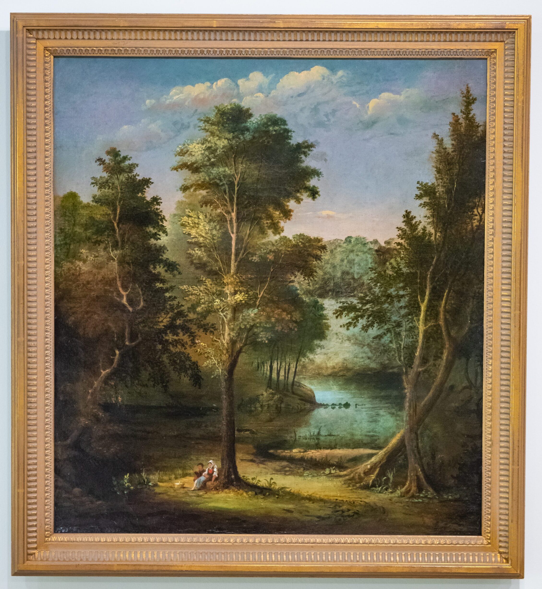 Framed painting of a landscapr with tall trees int he foreground and water in the background