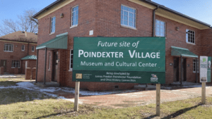 Brick building in the background with a sign out front that says: Future site of Poindexter Village Museum and Cultural Center being developed by James Preston Poindexter Foundation and Ohio History Connection