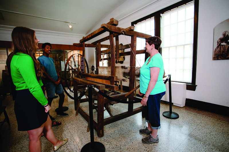 Museum staff member discussing historic textile loom with visitors at Campus Martius