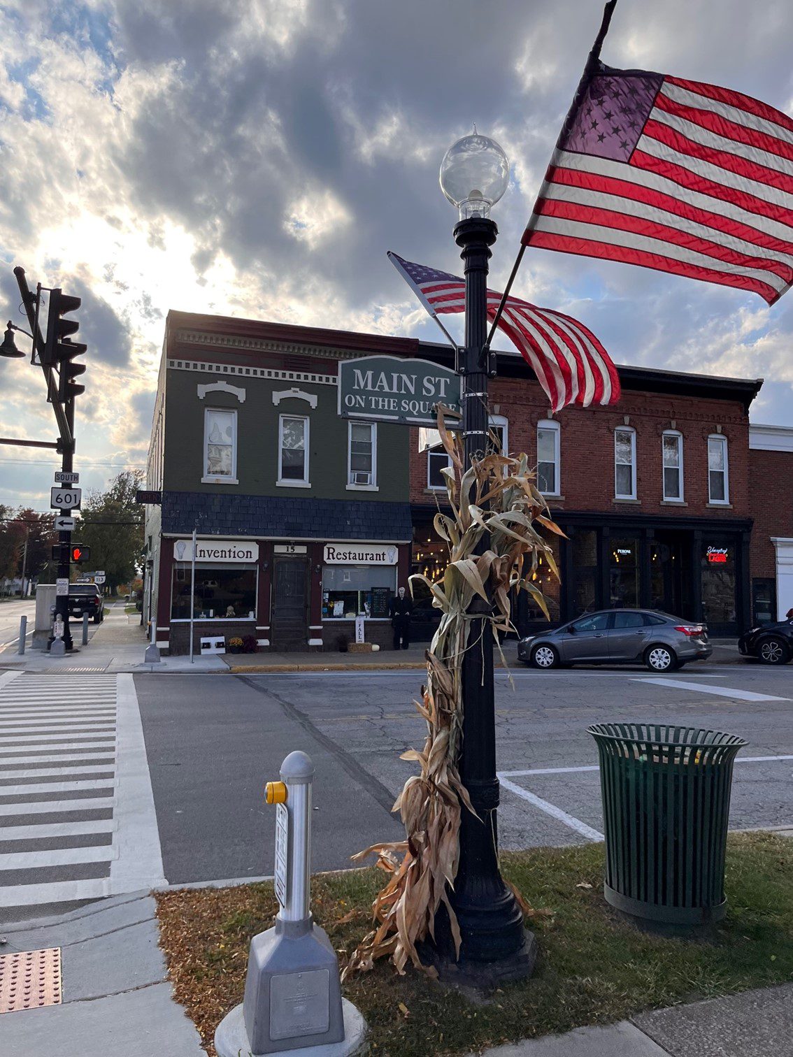 An outdoor image with an American Flag in the front; across the street in the back of the picture is a two-story brick building that has the words, "convention, restaurant, etc.