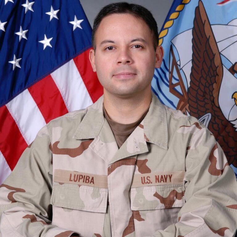 A man in a uniform is standing in front of an American Flag