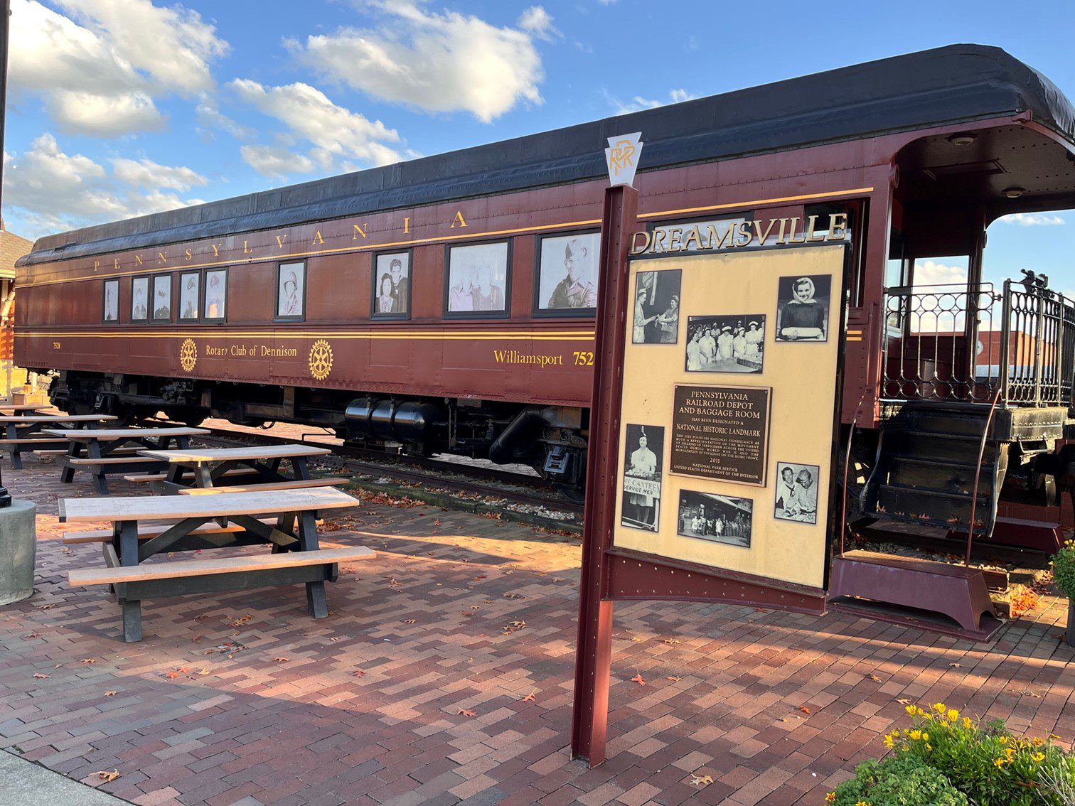 An outdoor picture of a Railroad car on a brick road with benches nearby.