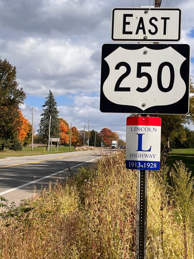 Outdoor image of a highway that shows yellow plants and vegetaion along the road and a sign upfront that says East 250