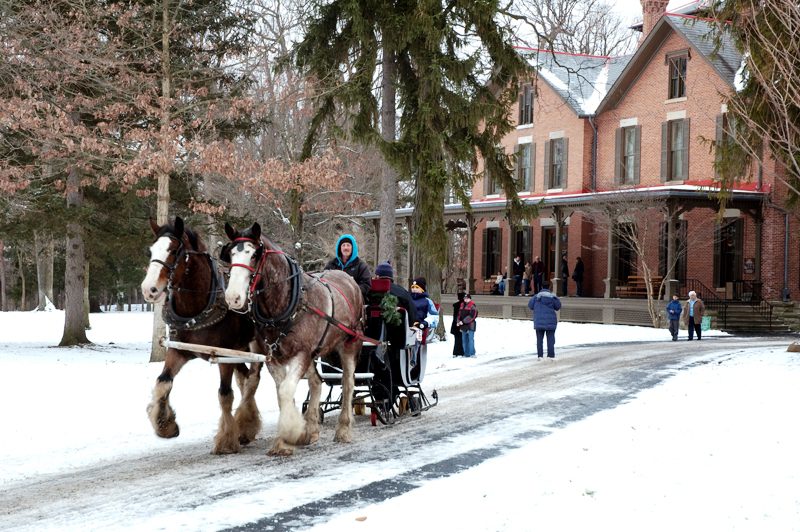 Two pairs of horses pull a sleigh in front of the walkway leading up to the Hayes home.