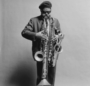 The featured musician, an African American blind male, is standing up and puffing his cheeks out a lot while he famously plays three reed instruments in perfect harmony.