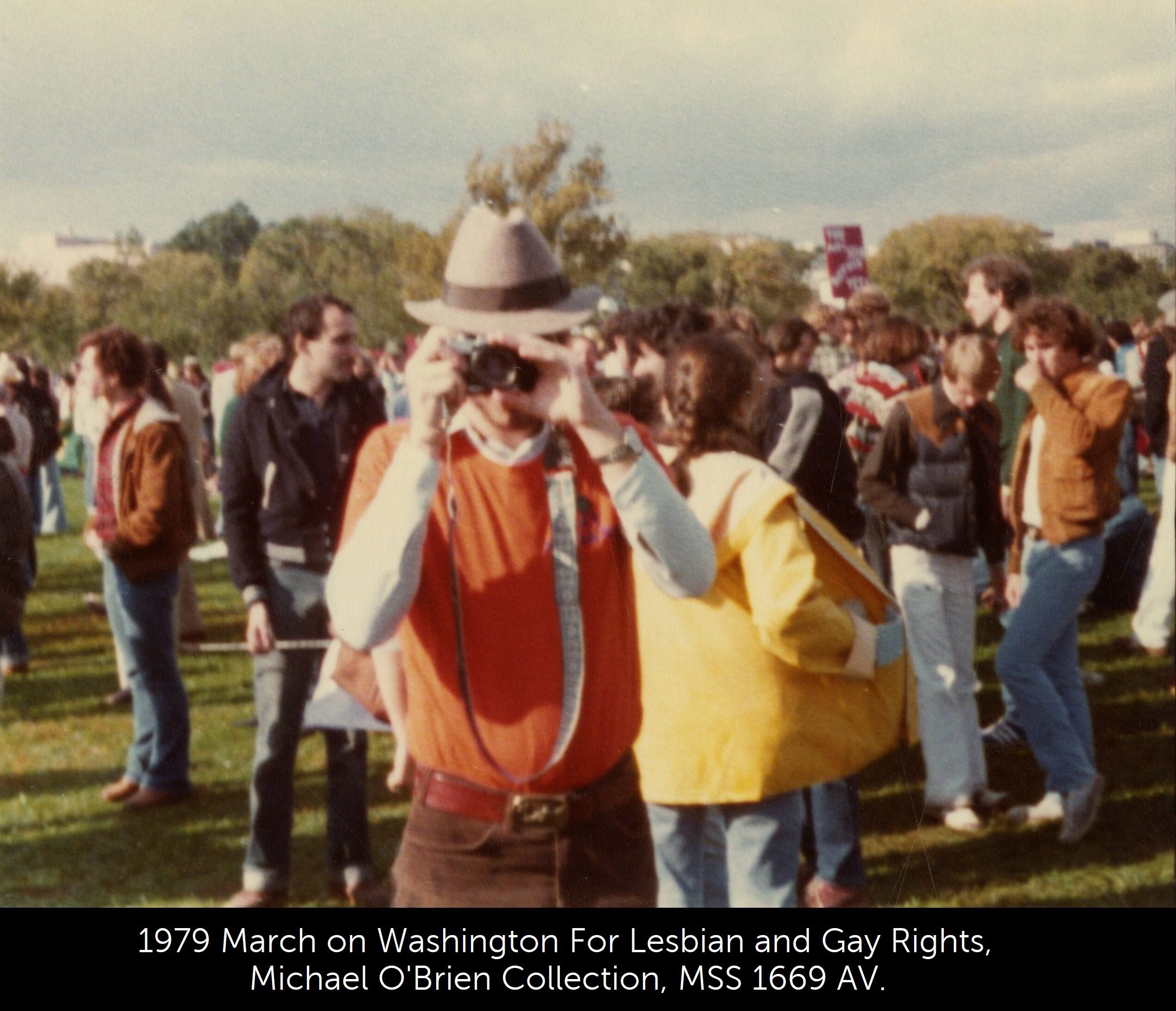 A photo of a person holding a camera up to their eye in front of several protesters