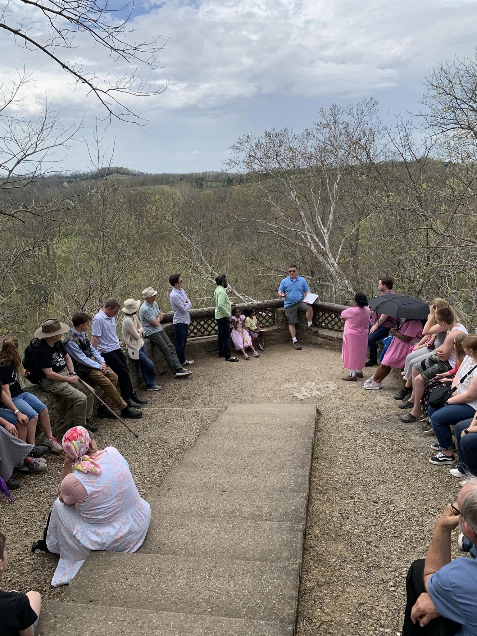 Group of people standing around an overlook onto the valley at Serpent Mound listening to tour leader Bill Kennedy.