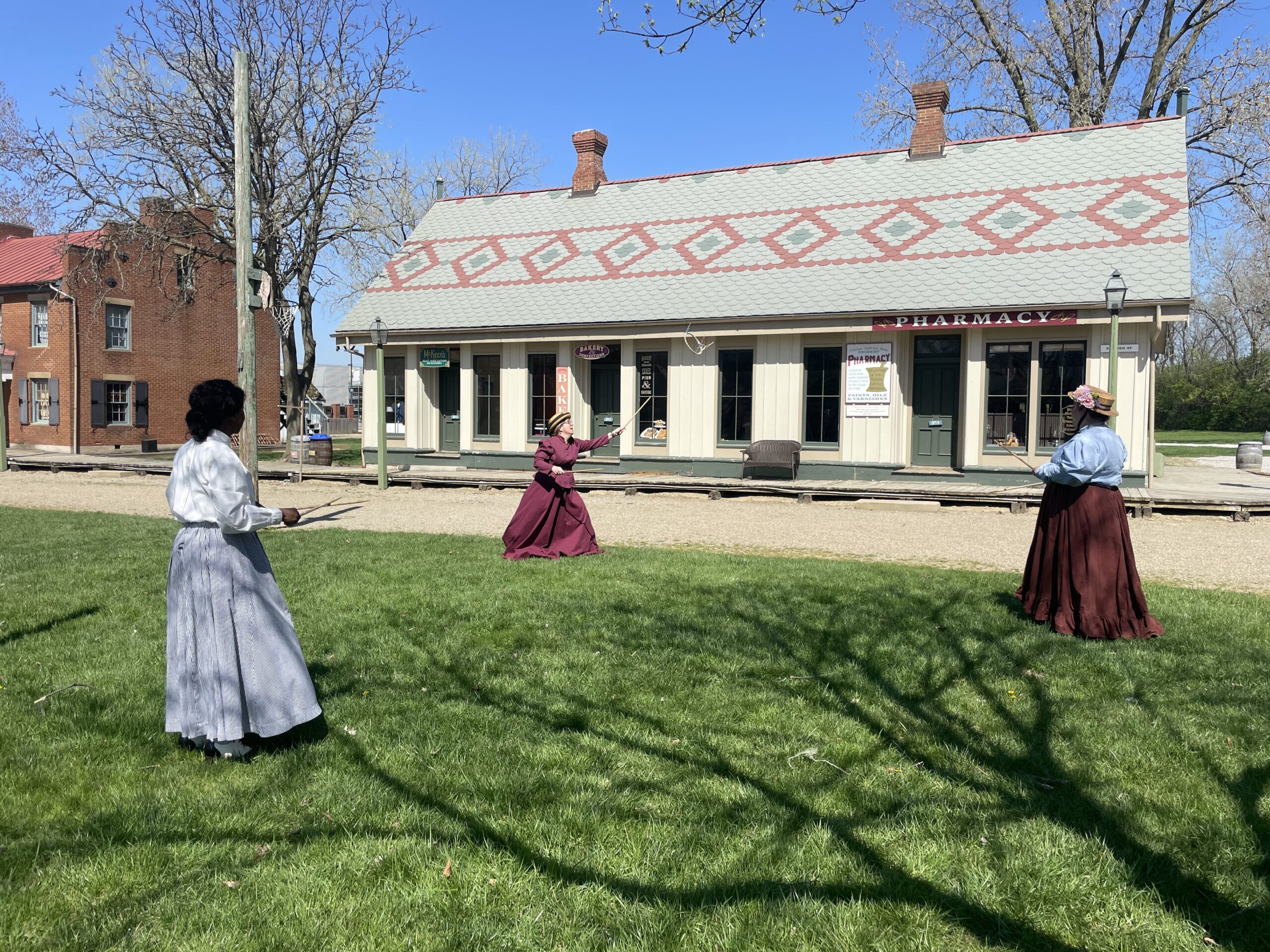 Three women in Ohio Village in 18902 period clothing playing a game of graces.