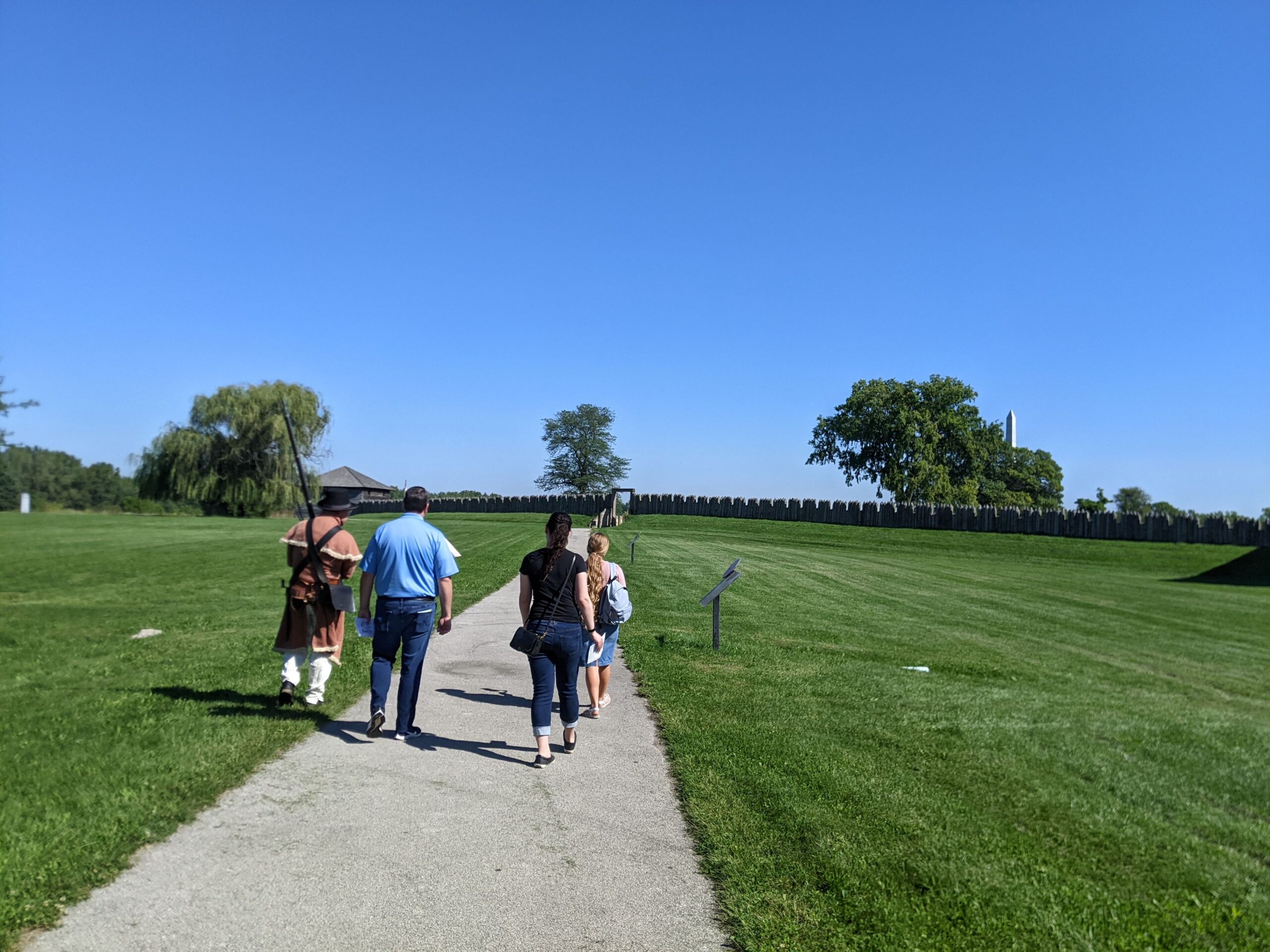 Four people on a paved path walking up to the wooden walls of Fort Meigs