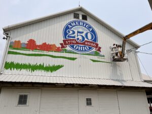 Person on a lift painting a mural on a white barn