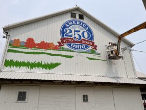 Person on a lift painting a mural on a white barn