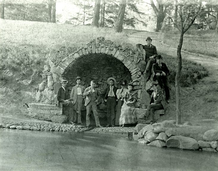 An 1892 photograph of a group of students at Ohio State University standing in front of a small grotto by Mirror Lake.