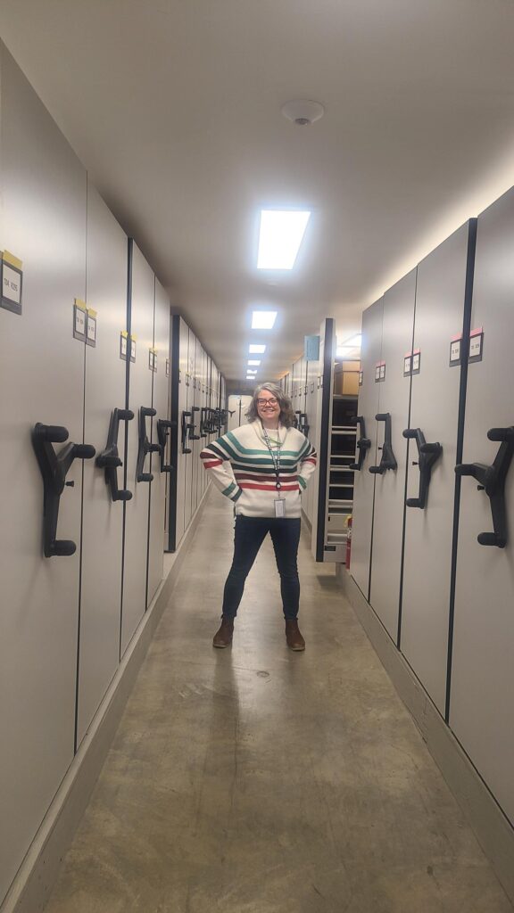 A woman standing in an aisle between shelving units.