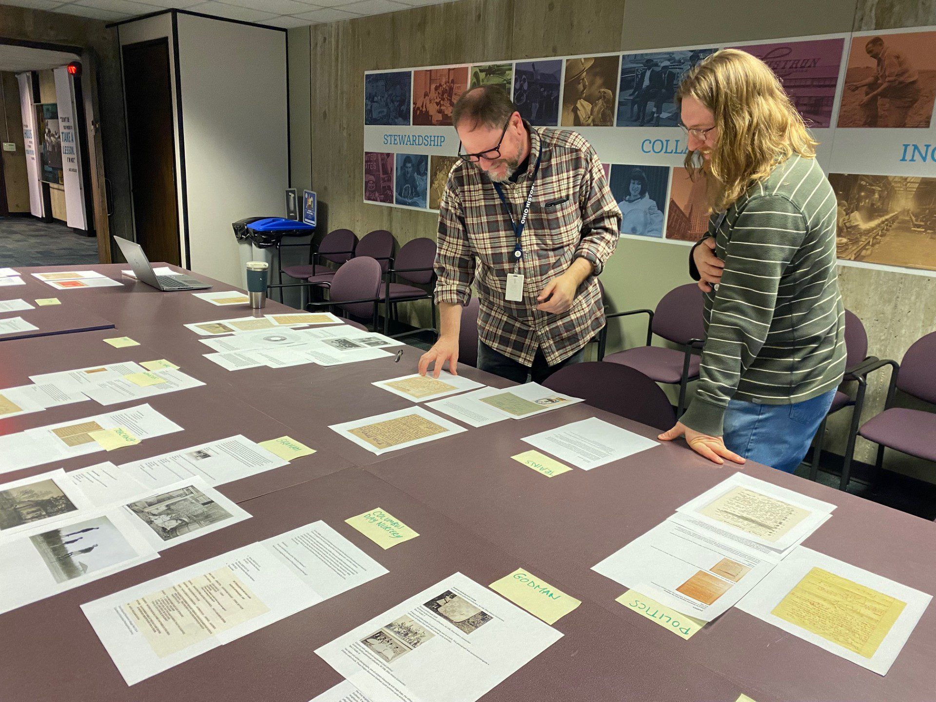 Two people standing over a table looking down at photos and captions that are laid across it.