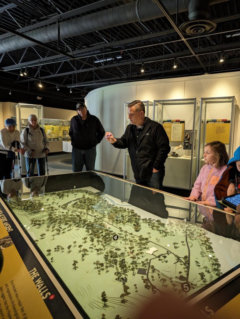 People standing over a case that contains a diorama showing the layout of Fort Ancient.