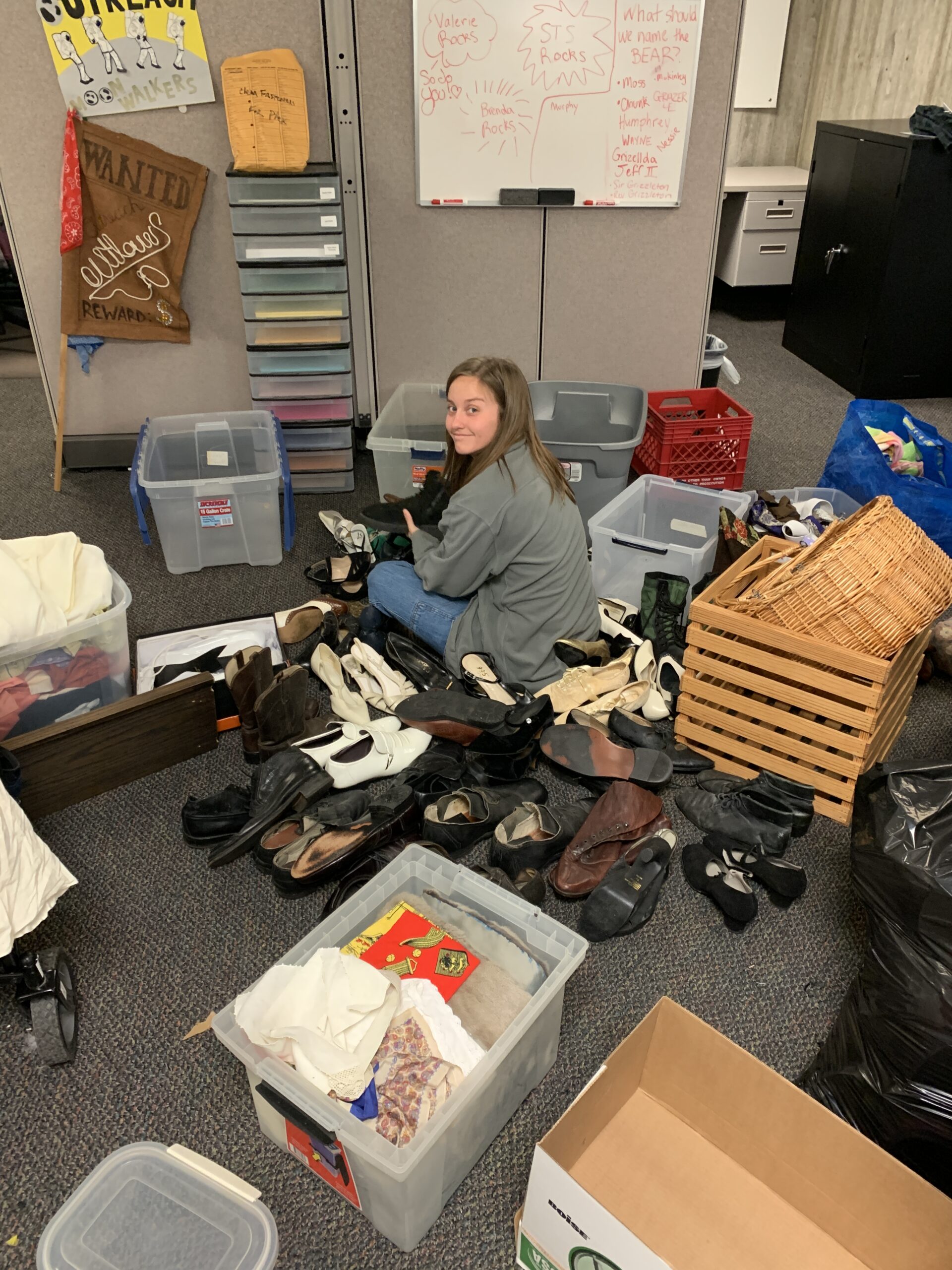 Woman in middle of photograph with bins and piles of costume pieces around her.