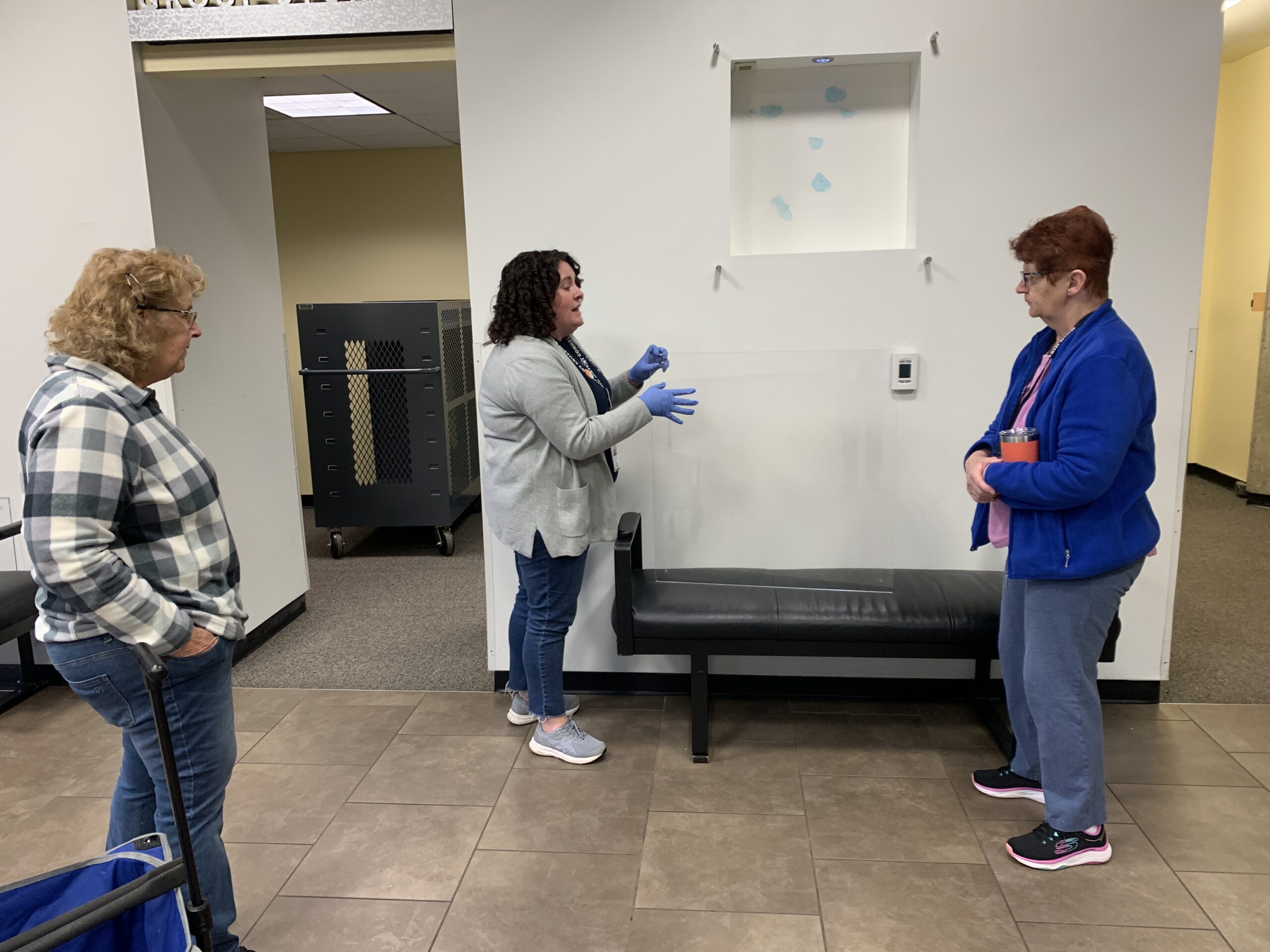 Three people working on a small in wall case in the front lobby of the museum. 