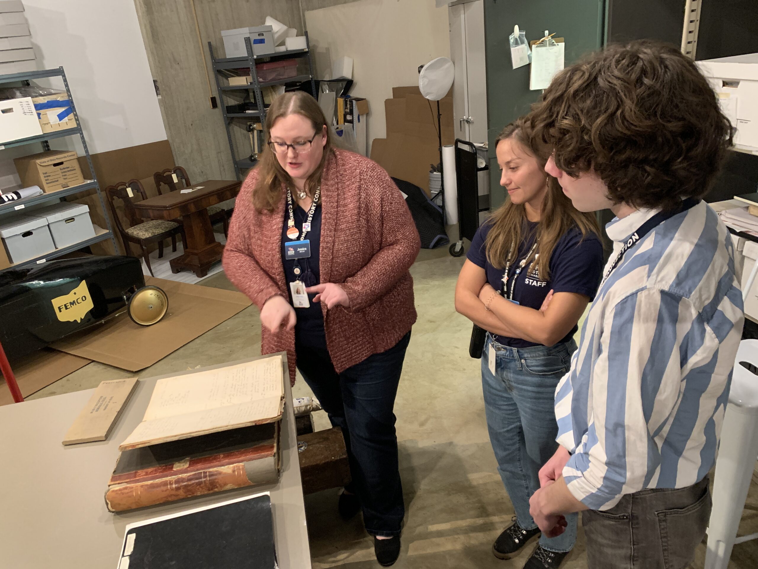 Three people looking at a large, old book on a table.