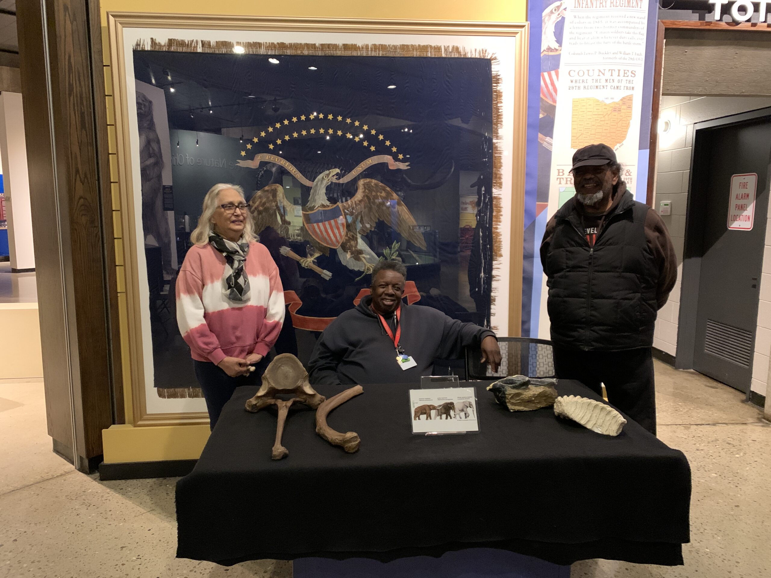 Three people sitting behind a table with large fossils on it. 
