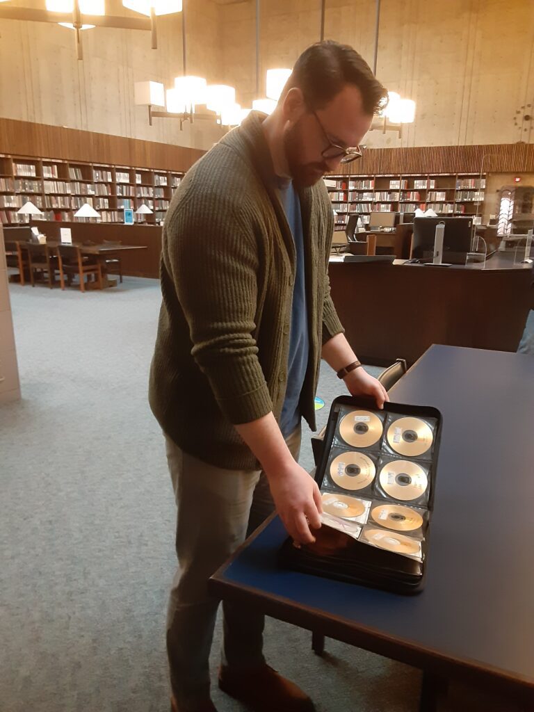 A person standing at a table looking at a CD organizer full of CDs.