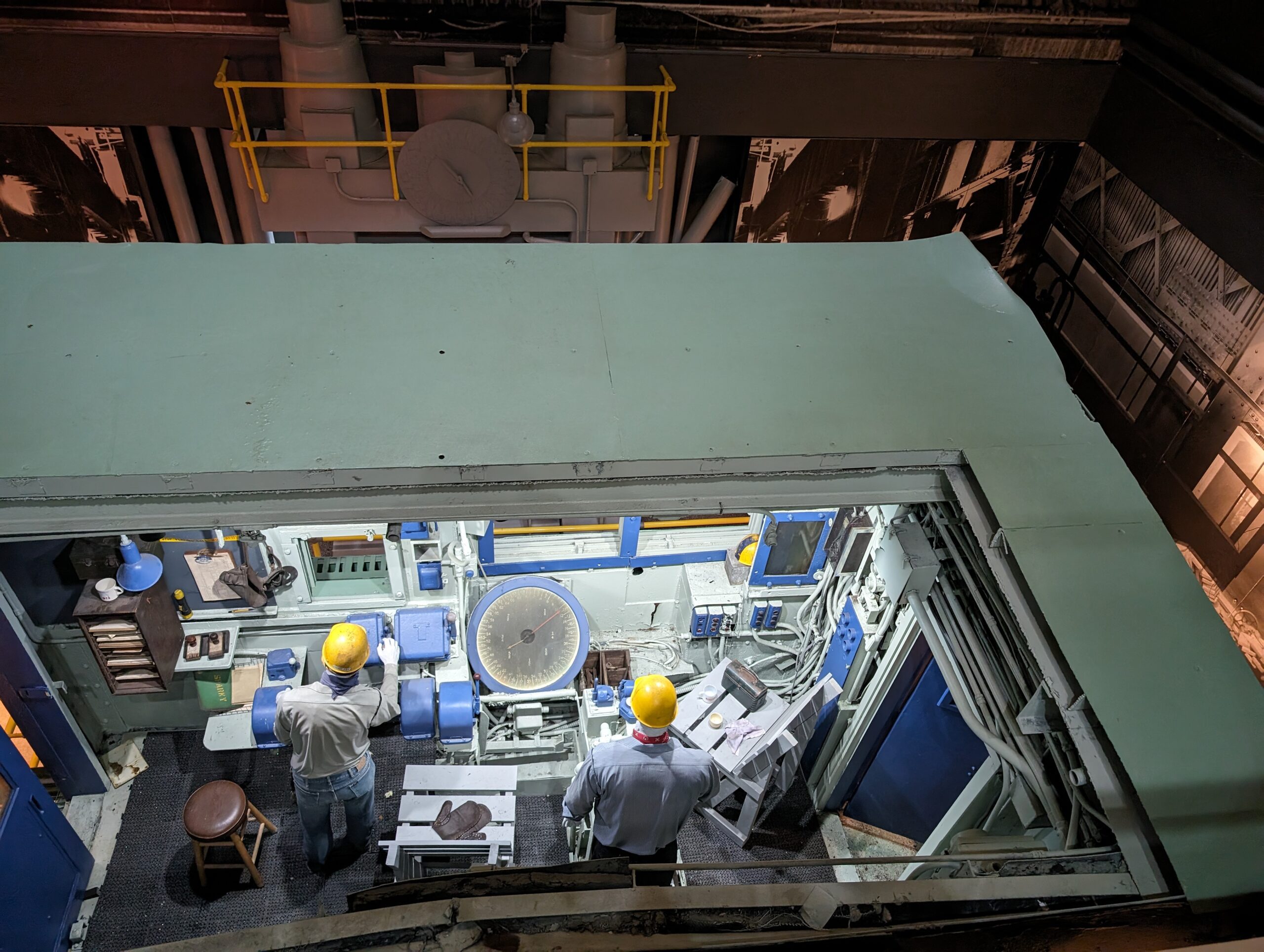 Image looking down into a steel industry control room with two figures working.