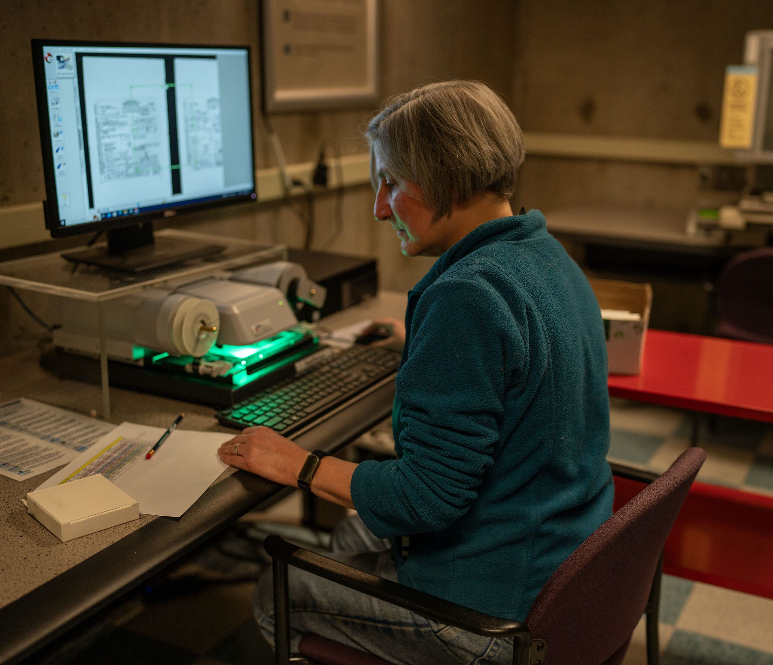 A person sitting at a computer referencing a sheet of paper.