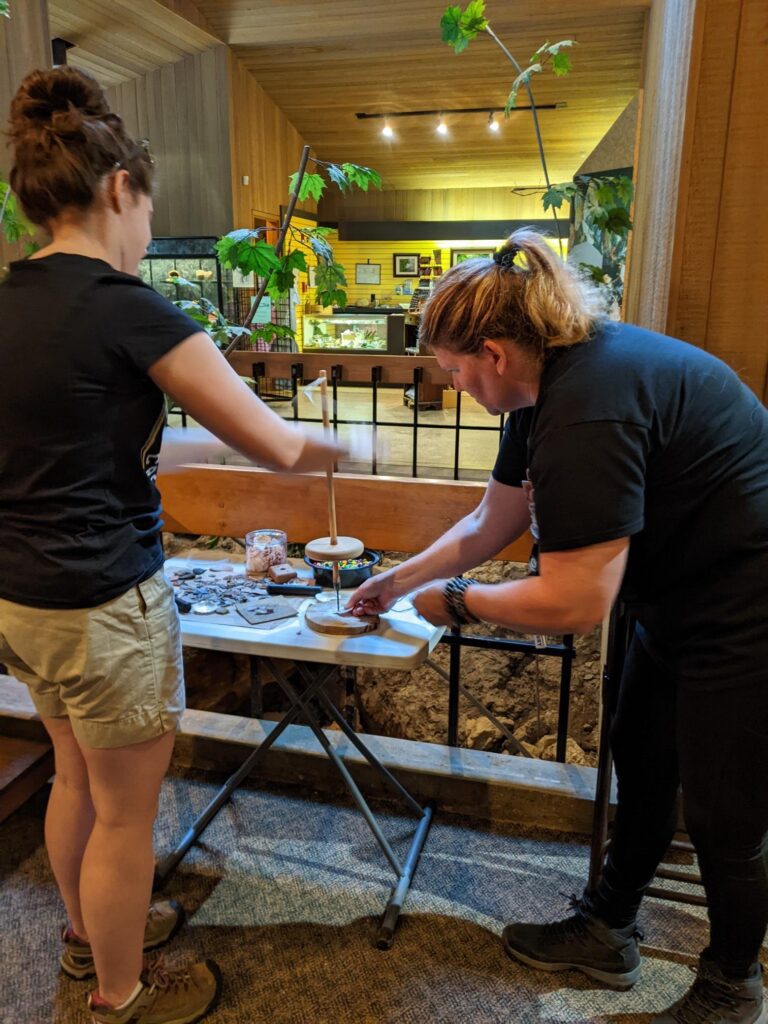 Two women showing how to use a small pump drill on a table at the Flint Ridge Center