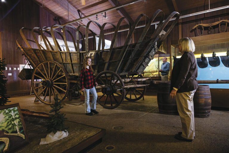 Image of girl with a Conestoga wagon at the National Road and Zane Grey Museum. Two other visitors are also looking around the museum.