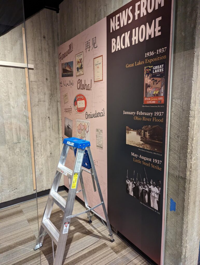 A photograph of a ladder in front of a museum exhibit panel. The panel text is partially readable.