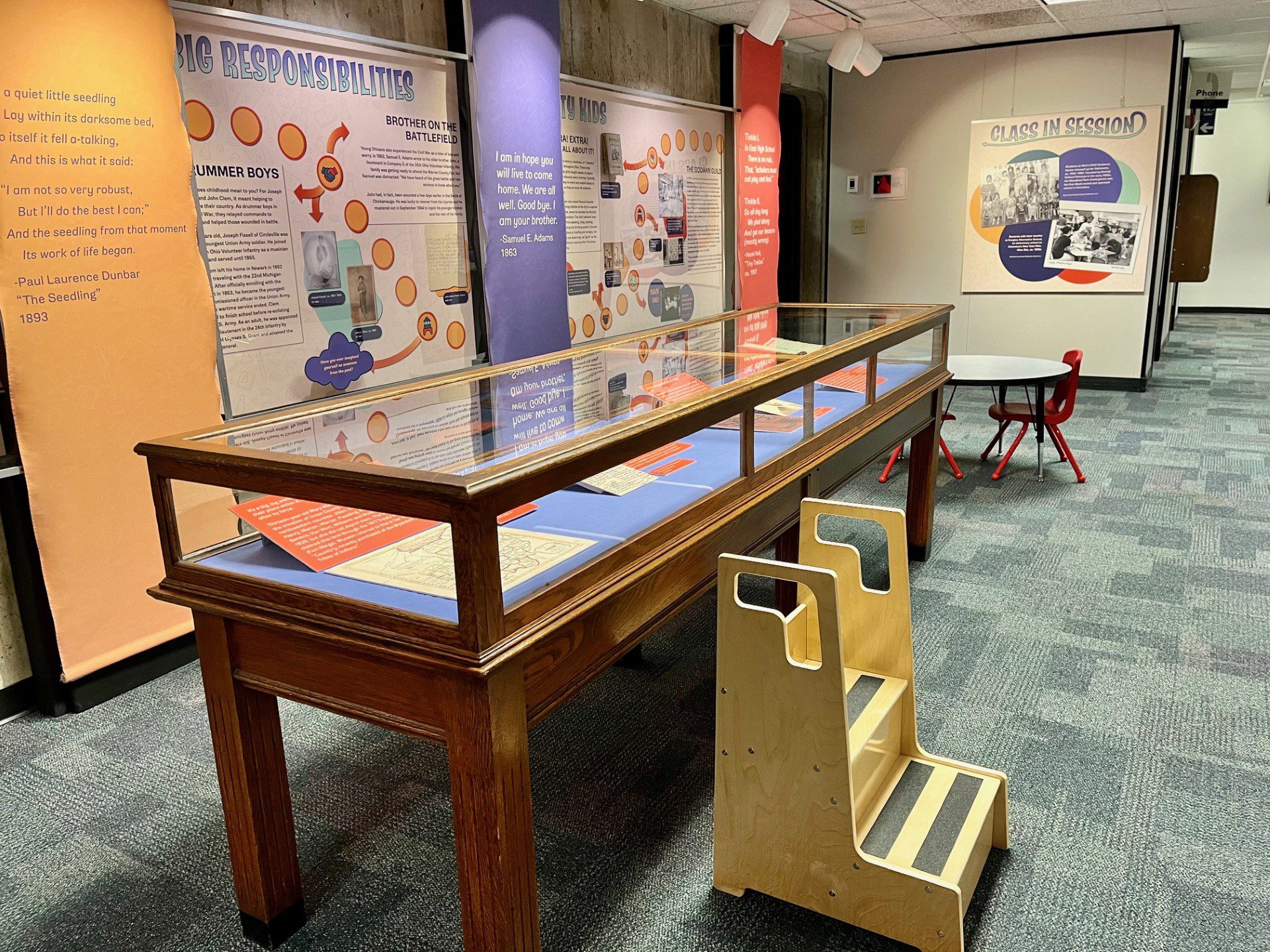 Color photograph of a museum exhibit featuring a display case and a step stool.