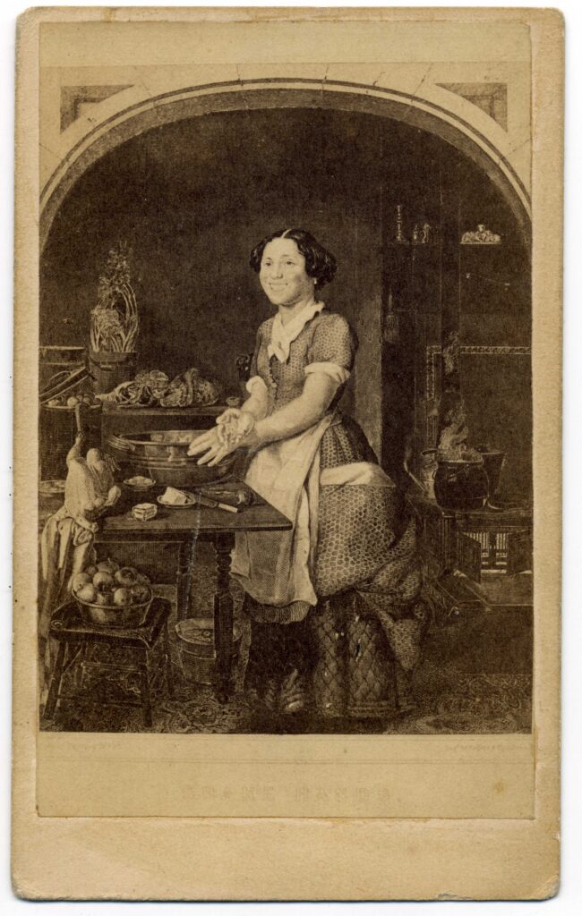 Black and white image of a smiling woman at work in a nineteenth-century kitchen who pauses her work to extend her dough covered hand to the viewer.