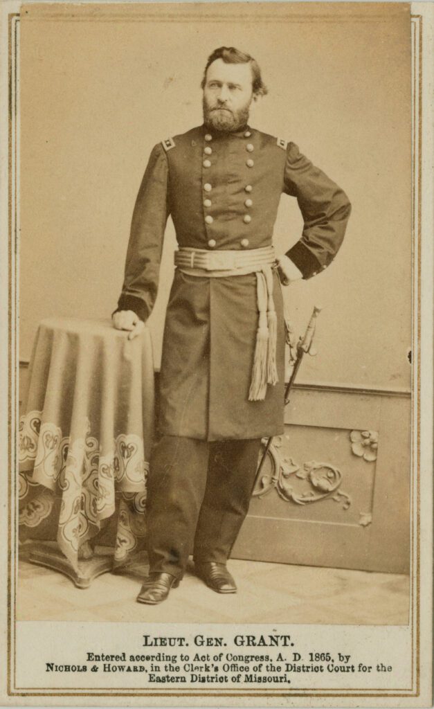 Photographic print of General Grant standing in his Civil War uniform with his right hand resting on a small, round side table.