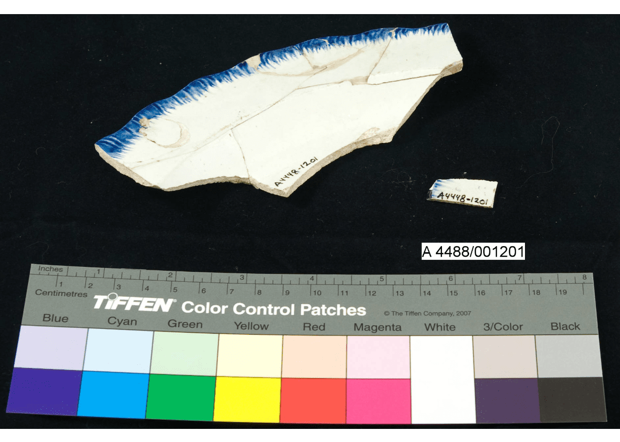 Broken edge of a white plate with a blue rim that has been partially glued back together