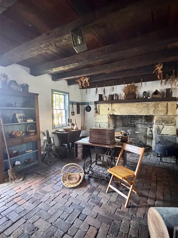 Room with a brick floor, fireplace in the back, shelves on the left side, and a table and chair in the center