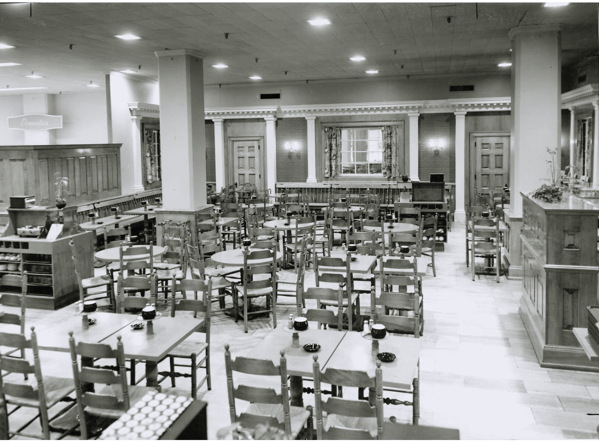 Black and white photograph of Colonial Room Restaurant at F. & R. Lazarus in the early 1950s. Image depicts a room of wooden tables with wooden ladderback chairs. 