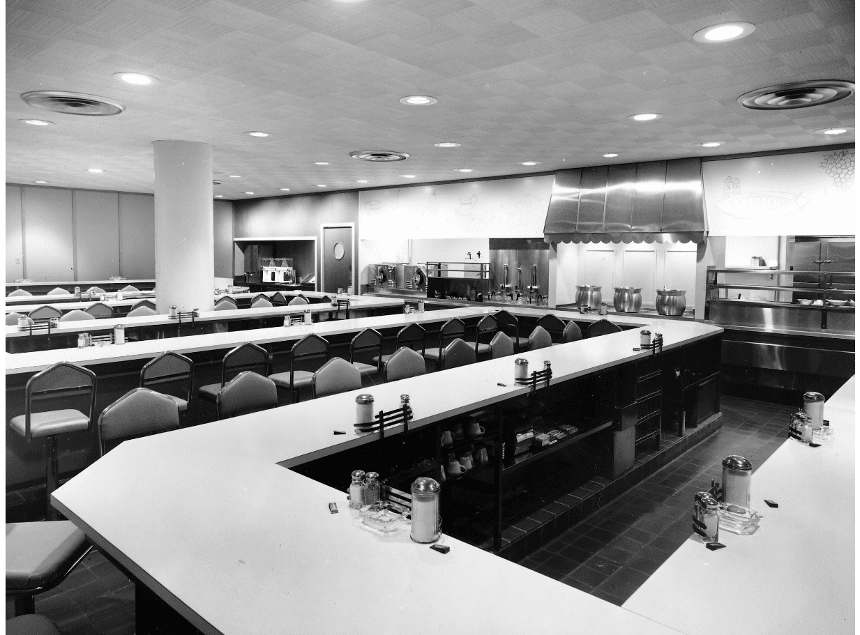 black and white photograph of Copper Kettle lunch counter at Lazarus depicting a long winding lunch counter with stools and kitchen visible behind the counter