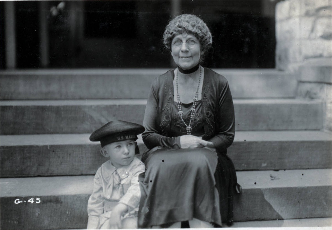 Dated 1920, this photograph shows Warren G. Harding's wife, Florence Kling Harding, sitting on the porch steps of her home in Marion, Ohio with a young boy in a U.S. Marines hat.